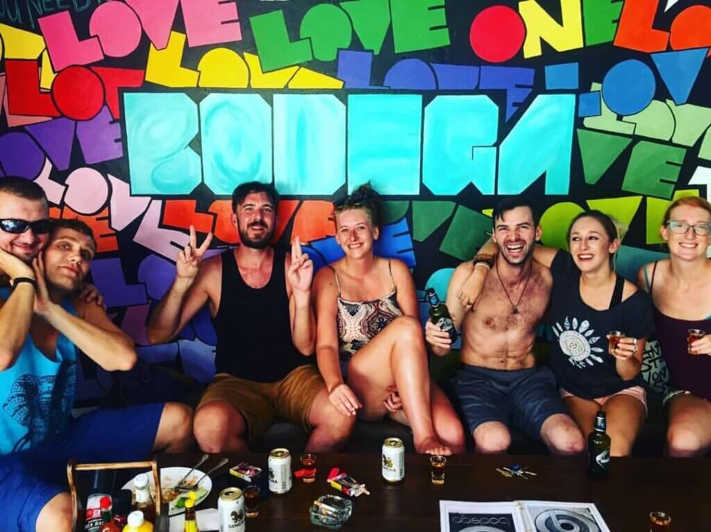 group of friends posing for a photo in front of graffiti wall saying bodega
